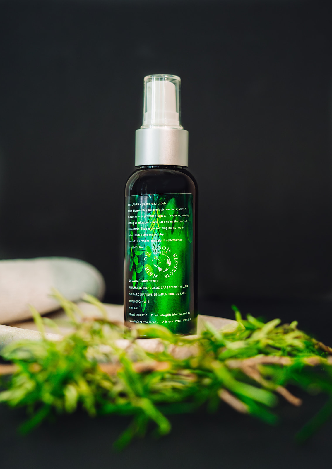 Moon Blossom Hair Oil bottle standing upright on a wooden board with fresh greenery